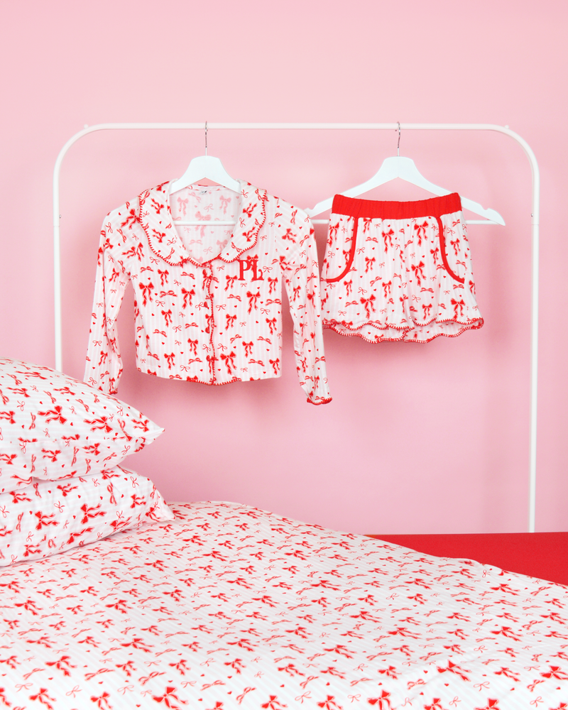 Set roze en wit gestreepte meisjes P.Louise kerstpyjama's met strik op hangers in een roze slaapkamer met bijpassend beddengoed