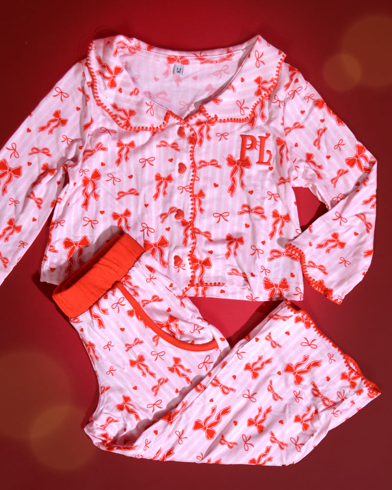 Set roze en wit gestreepte kerstpyjama's voor kinderen met rode strikjes erop tegen een rode achtergrond