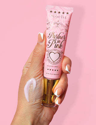 A hand holding a tube of P.Louise Partner In Pink Sculpting Primer with a pink swipe of the product on the skin
