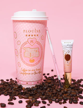A product image featuring a double-ended eyebrow pencil next to a tube of eyebrow gel, displayed on a pink surface with coffee beans scattered around. The background has a pink coffee cup with branding elements.