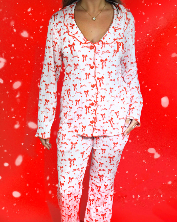 Shot van het lichaam van een vrouw, gekleed in een feestelijke set roze en wit gestreepte pyjama's met rode strikjes erop tegen een rode achtergrond en sneeuwvlokken