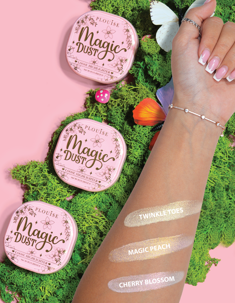 Drie compacte losse markeerstiften met het opschrift Magic Dust in de kleuren Twinkle Toes, Magic Peach en Cherry Blossom, weergegeven op een arm met een bloemenachtergrond.
