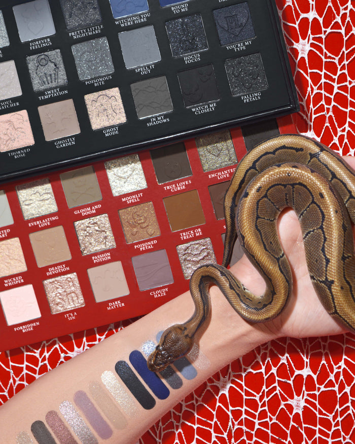 P.Louise Mystic Moonlight halloween oogschaduw & make-up palet met swatches op een arm met een slang eromheen gewikkeld tegen een rode spinnenwebachtergrond