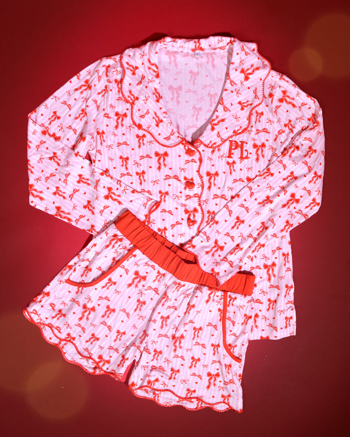 Afbeelding van roze en wit gestreepte kerstpyjama's voor volwassenen met rode strikontwerpen op een rode achtergrond