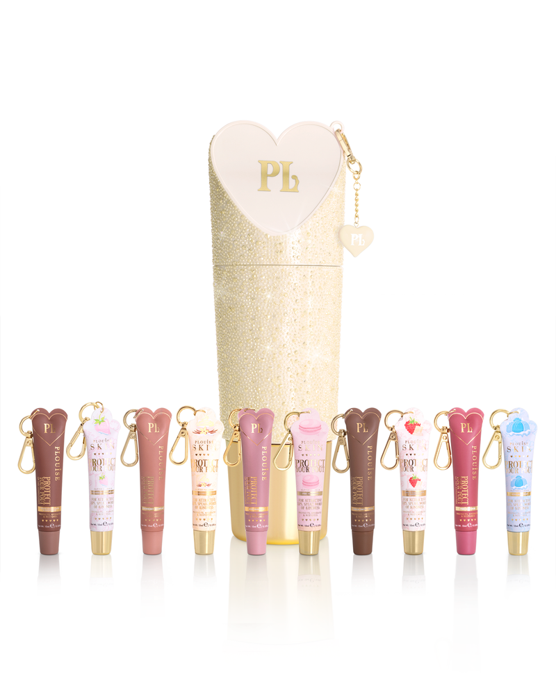 Een set P.Louise beschermt je pruillip-lipconditionertubes in verschillende tinten, gerangschikt voor een hoge, glitterende crèmekleurige cilindrische doos met een hartvormige ritssluiting. Aan elke buis is een kleine gouden sleutelhanger bevestigd.