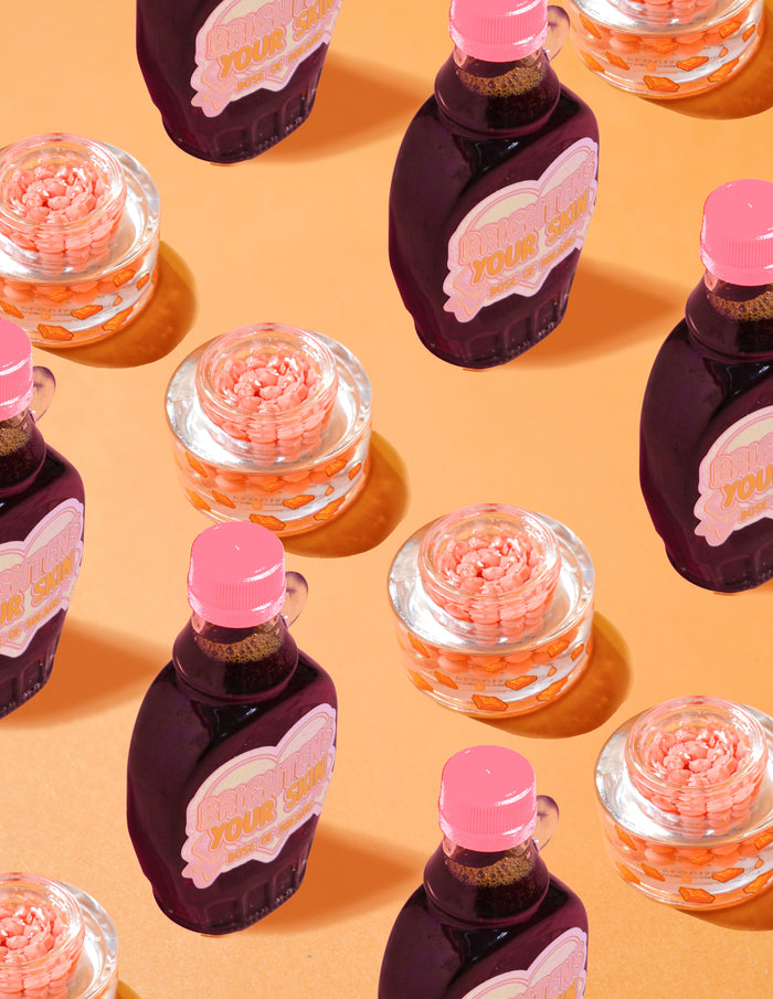 Doorzichtige containers met P.Louise Dose of Dreams Vitamine C Capsule Cream met oranje capsules erin omgeven door paarse en roze siroopflessen op een oranje achtergrond
