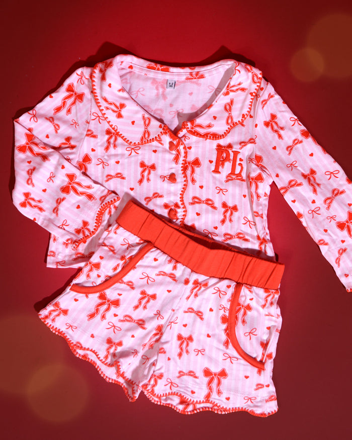 Set roze en wit gestreepte kerstpyjama's voor kinderen met rode strikjes erop tegen een rode achtergrond