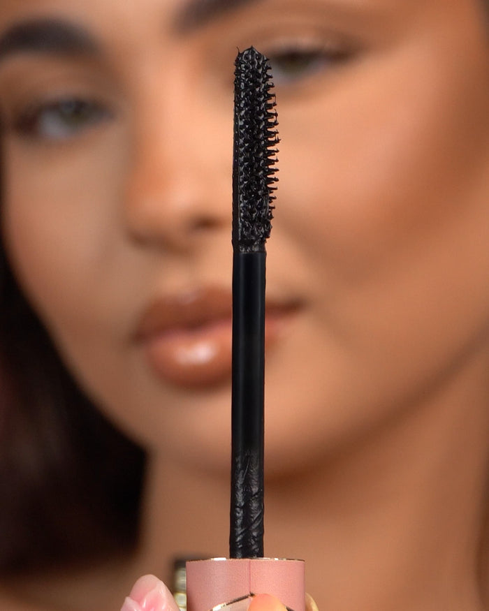 Close-up van een P.Louise Tearproof waterproof mascara-staafje dat voor een wazig gezicht wordt gehouden